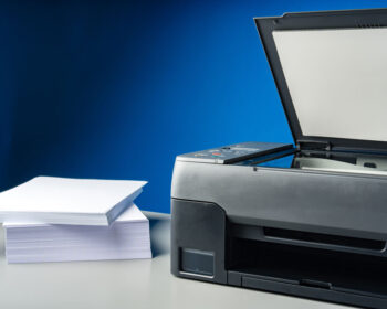 A printer on a table with white paper to the side.