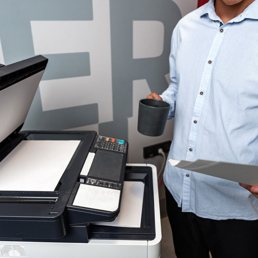 Man holding a coffee cup standing at copier machine making copies.